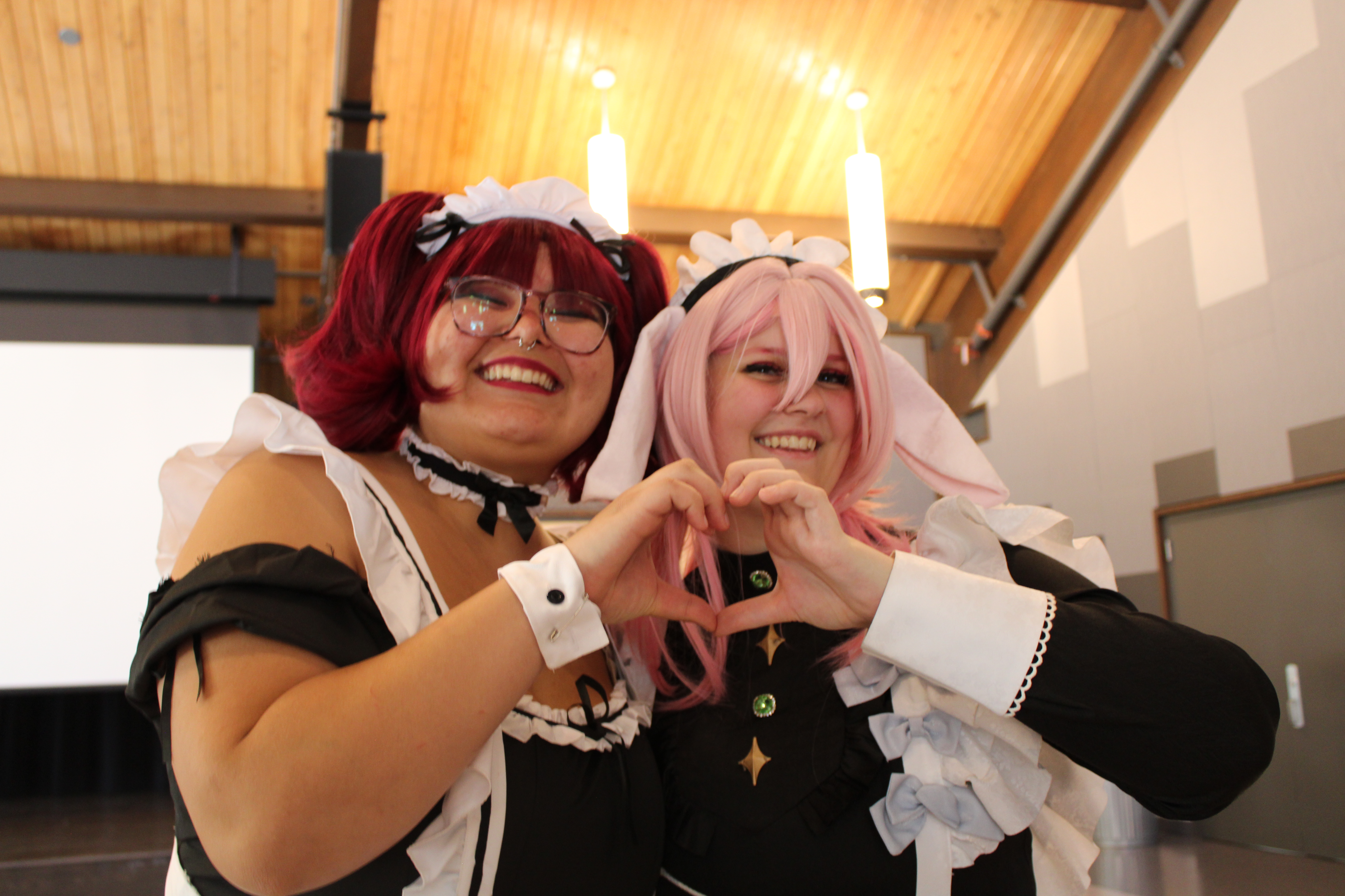two people in maid costumes forming a heart with their hands in the convention center